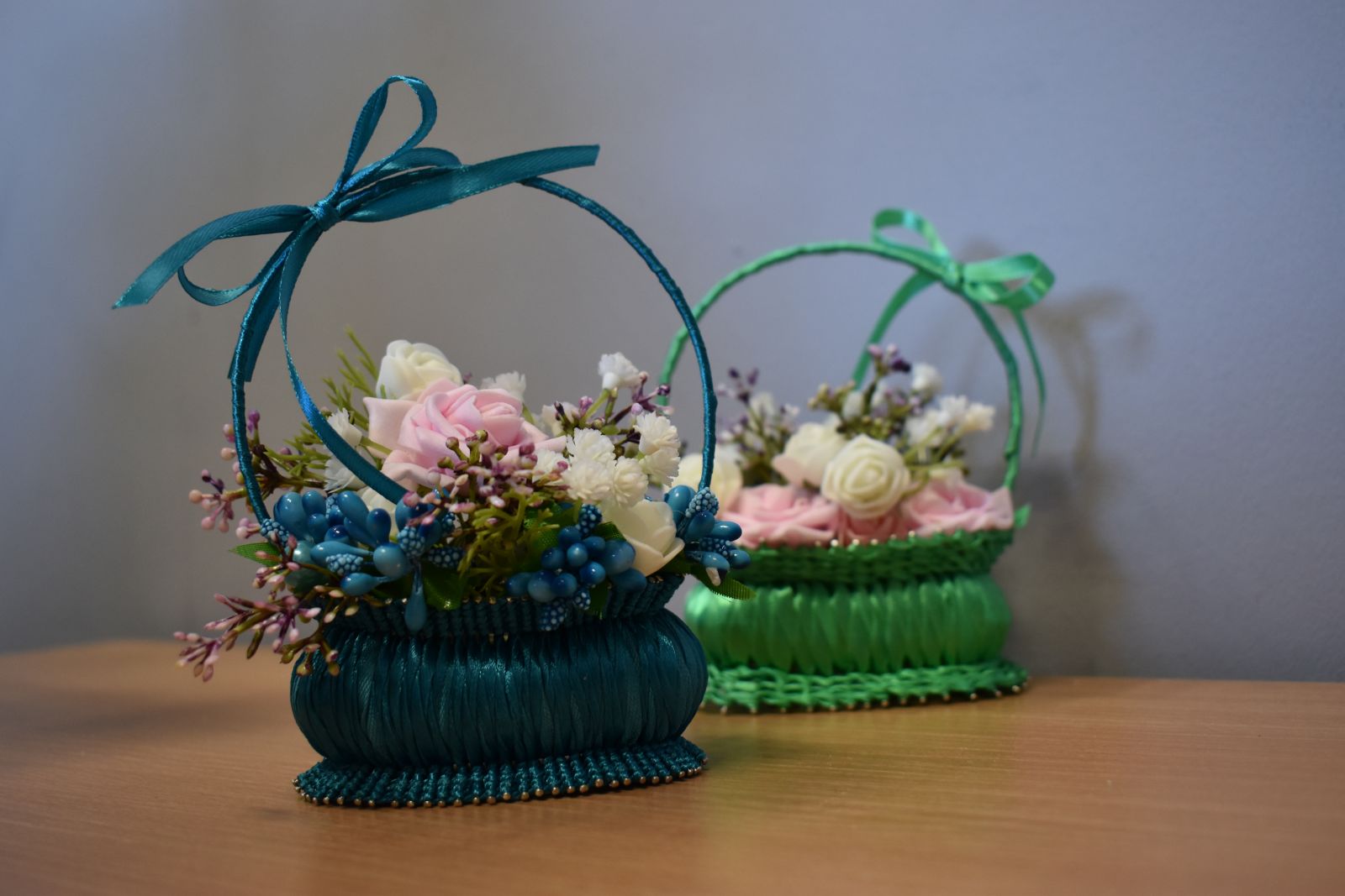 Niebieskie tło, na stoliku koszyczki wykonane z mydełka ozdobione wstążką i kwiatami